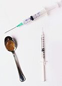 Two syringes and a spoon containing brown substance