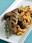 Lamb sausages with white beans garnished with thyme sprig