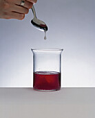 Clear liquid dripping into a beaker containing red liquid