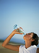 Woman drinking from a bottle of water against a blue sky