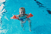 Boy in pool wearing armbands and treading water