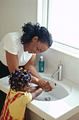 Woman washing young girl's hands in washbasin