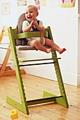 Laughing blonde baby sitting in a green highchair