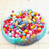 Boy lying on back amongst coloured balls in plastic pool