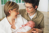 Couple smiling and leaning over baby held in mother's arms