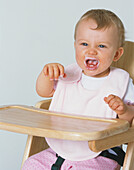 Baby girl wearing bib sitting in high chair with raised arms