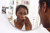 Woman taking off make-up in front of a bathroom mirror