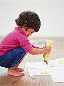 Girl squeezing yellow paint from bottle onto white paper
