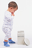 Toddler standing next to a biscuit jar, side view