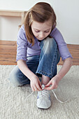 Girl tying shoe lace, kneeling on rug
