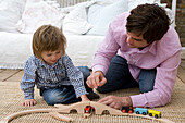 Boy and man playing together with wooden train set