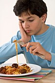 Boy holding fork over plate of spaghetti and meatballs