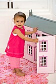 Girl in pink clothes opening door to doll's house