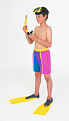 Boy wearing swimming trunks and fins holding a snorkel