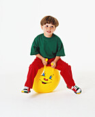 Boy in red and green clothes sitting on yellow rubber ball