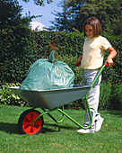 Girl carrying a full sack of rubbish on a wheelbarrow