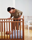 Woman looking down at baby lying in cot