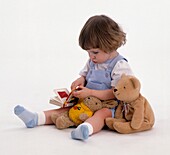 Girl sitting on floor with teddy bear, toy rabbit and book