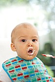 Baby boy with food smeared around his mouth, wearing a bib
