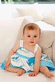 Baby girl in blue and white dress sitting on sofa