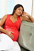 Pregnant woman using earphones with eyes closed on a sofa