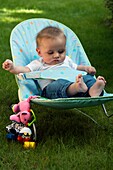 Baby boy sitting strapped into a chair in a garden