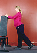 Pregnant woman holding top of raised fitness bench