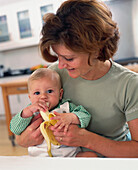 Mother holding baby as he eats a banana