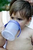Baby boy drinking from plastic beaker