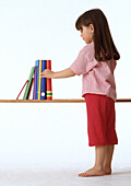 Girl in pyjamas taking book from a shelf