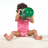 Baby girl sitting on rug holding up green bucket