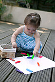 Baby girl sitting on decking painting with crayons
