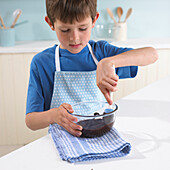 Boy stirring melted dark chocolate in a glass bowl