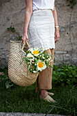Woman carrying basket bag with white bouquet of peonies, snowball, motherwort and grasses