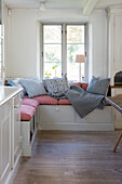 Eingebaute Sitzbank mit Kissen und Decke vor Fenster in der Wohnküche