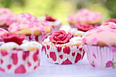 Kirschmuffin mit roter Marzipanrose und Muffins mit rosa Glasur und Zuckerherzen