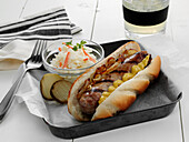 A grilled Bratwurst sausage on a bun with yellow mustard and sauteed onions served with coleslaw and pickles