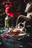 Black tea being poured from a porcelain teapot into a glass cup