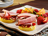 Ham crostini appetizers with tomato, vegetables and mozzarella cheese on rounds of corn bread