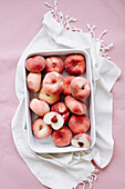 White peaches in a bowl on a pink background