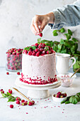 Raspberry cake with a hand putting a raspberry on top