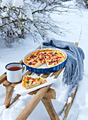 Quiche mit Paprika, Schinken und Ricotta auf Schlitten im Schnee
