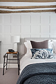 Doppelbett im Gästezimmer mit weiß getäfelter Wand und Holzbalkendecke