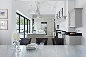 View over aluminium-clad table to kitchen island and industrial pendant lights