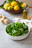 Baby spinach in a bowl, lemons and garlic in the background