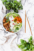 Chicken noodle bowl with zucchini, grated carrot and fresh herbs