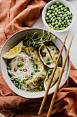 Gyoza dumpling soup with thin rice noodles, broth, peas, chili, sprouts and a slice of lemon