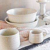 White matching stoneware mugs, plates, bowls with white pillar candles, white flowers in a vase