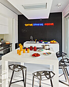 White table with designer stools and kitchen island in front of black wall with neon writing