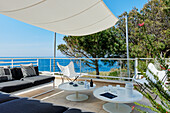 Terrasse mit weißen Tischen, Klassikerstühlen, Sitzbank, Sonnensegel und Meerblick